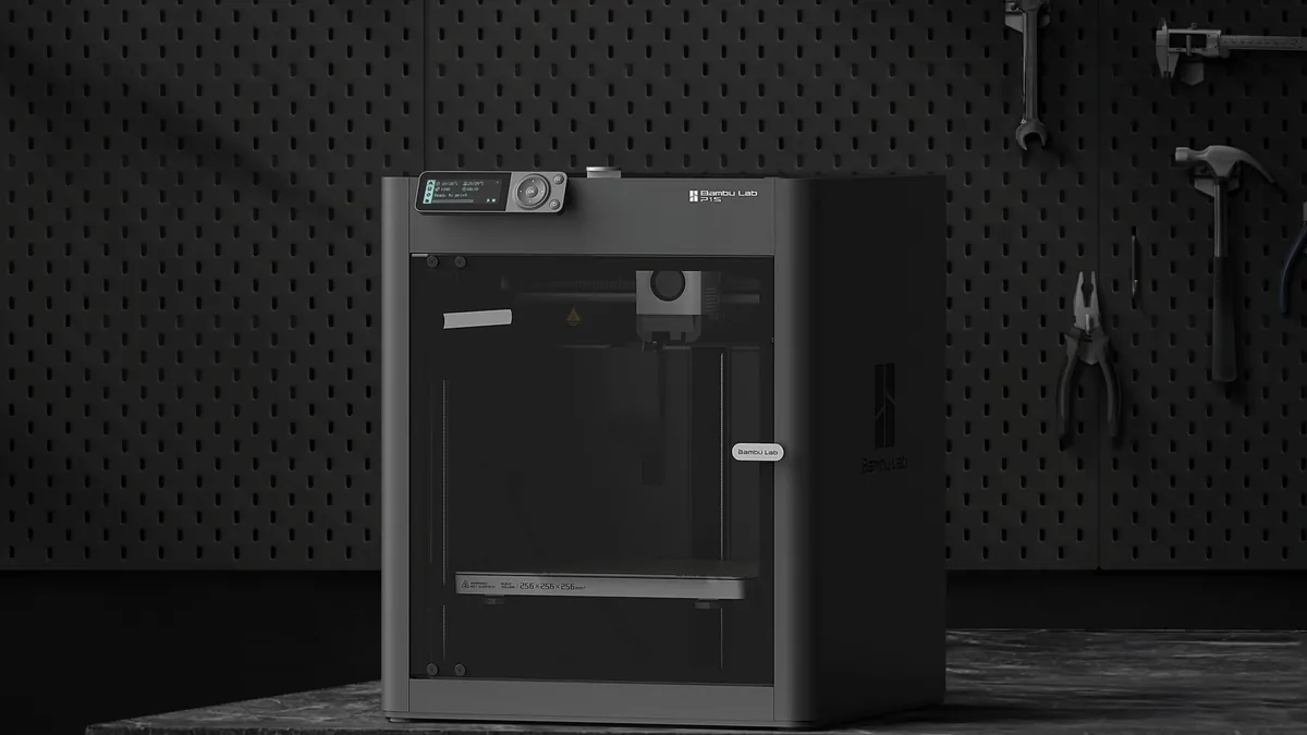 Impressora 3D Bambu Lab P1S, fechada e cinza-escura, sobre um bloco de pedra diante de uma parede perfurada com ferramentas penduradas