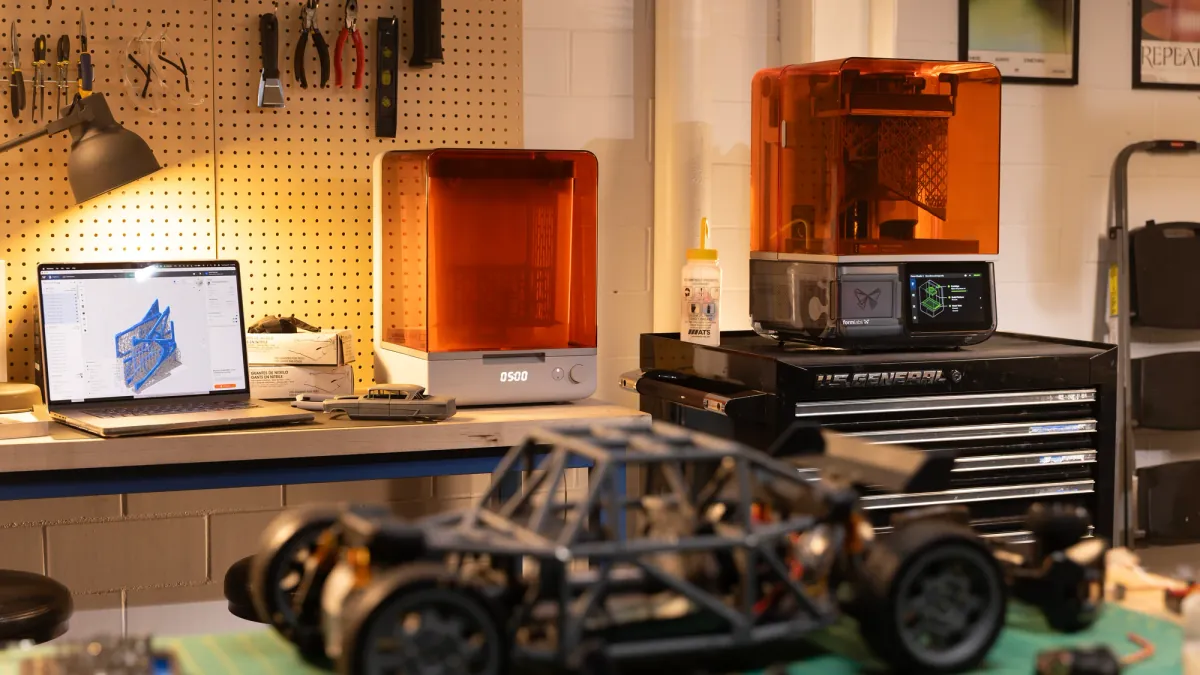 Impressora de resina Formlabs Form Studio 1, de tampa laranja translúcida e tela sensível ao toque, sobre um gaveteiro de ferramentas numa oficina, com a estação Form Studio Wash+Cure na bancada ao lado
