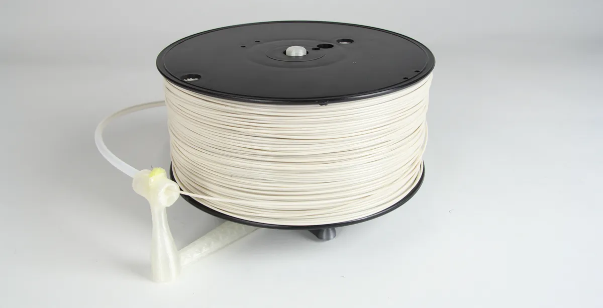 Rolo de filamento branco em um suporte, com o fio saindo por um guia impresso em 3D