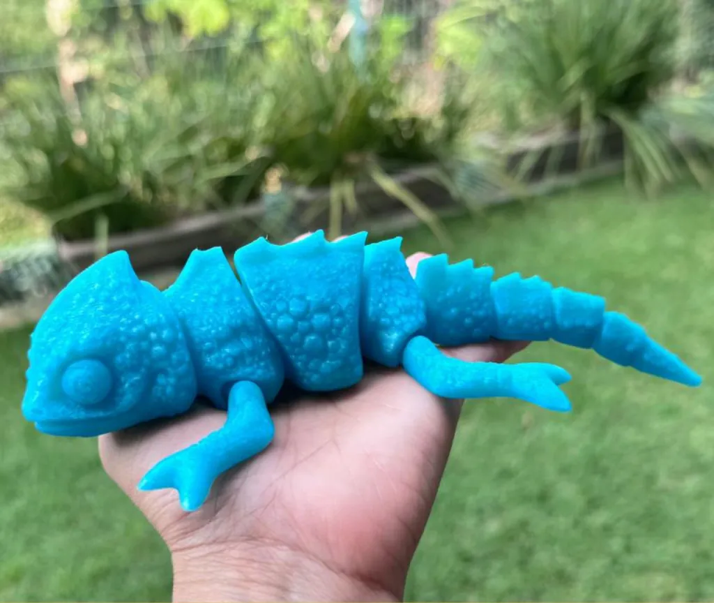 Lagarto articulado azul impresso em 3D na palma de uma mão, brinquedo da marca Migles Mini Labs