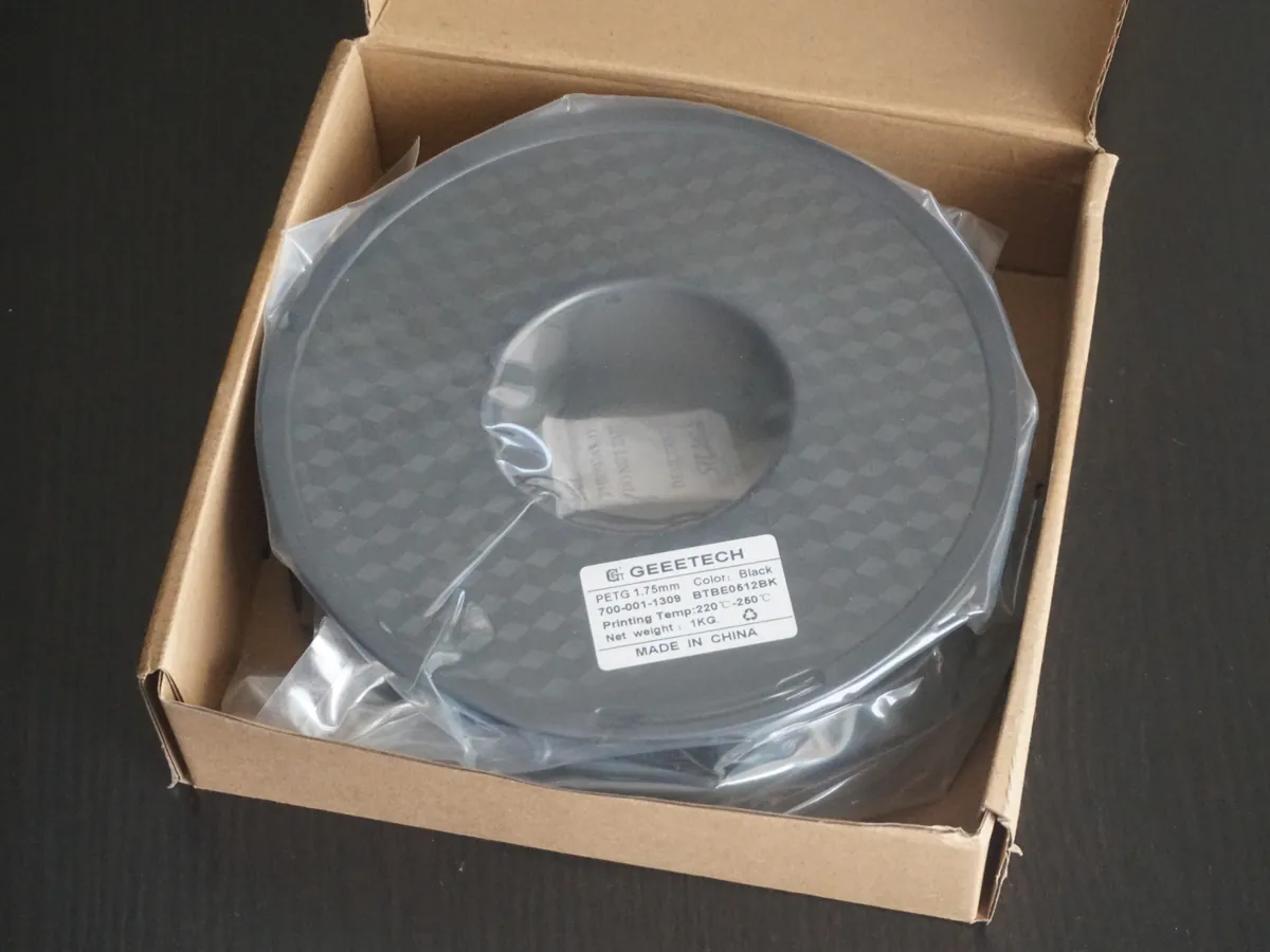 Rolo de 1 kg de filamento PETG preto na embalagem de papelão, com a etiqueta indicando temperatura de impressão de 220 a 260 °C