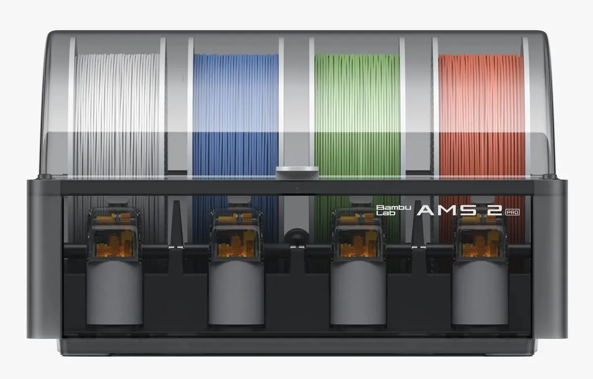 Alimentador AMS 2 Pro da Bambu Lab visto de frente, com tampa transparente e quatro bobinas de filamento branco, azul, verde e vermelho lado a lado sobre os alimentadores