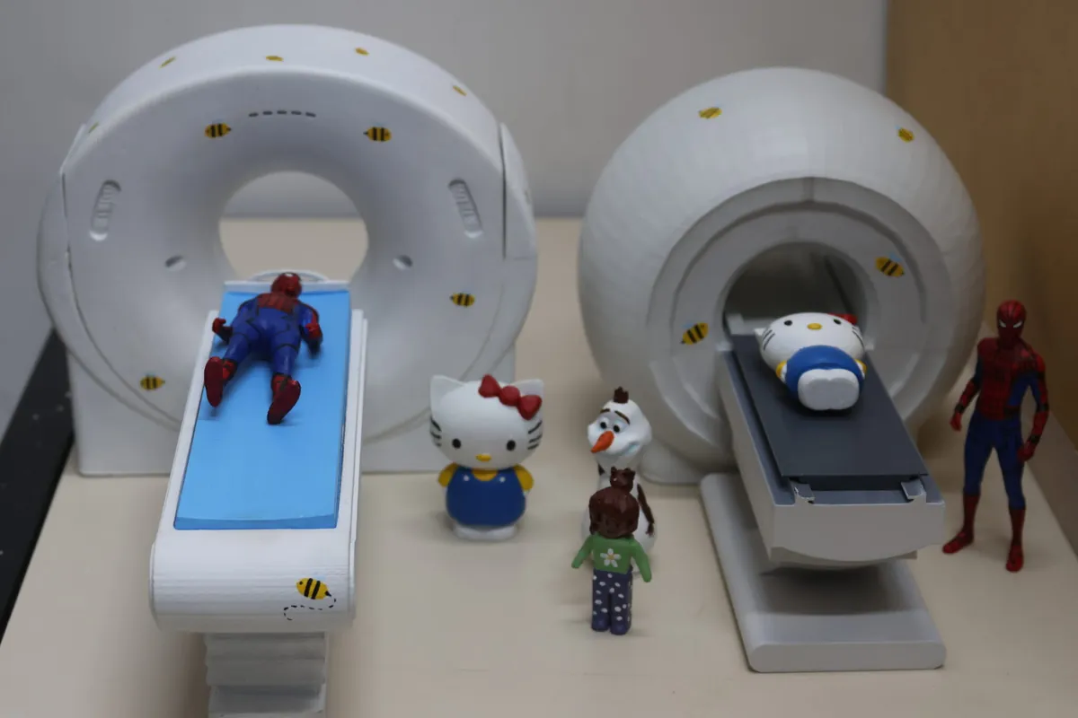 Maquetes impressas em 3D de um aparelho de ressonância magnética e de um tomógrafo, com bonecos posicionados na maca, produzidas pela Faculdade de Medicina da UFMG